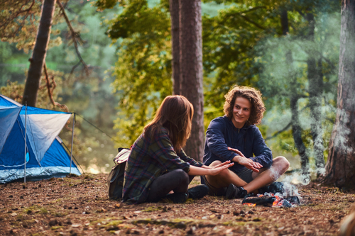 happy young couple sitting warming near campfire camp forest travel tourism hike concept 1 Skyteach